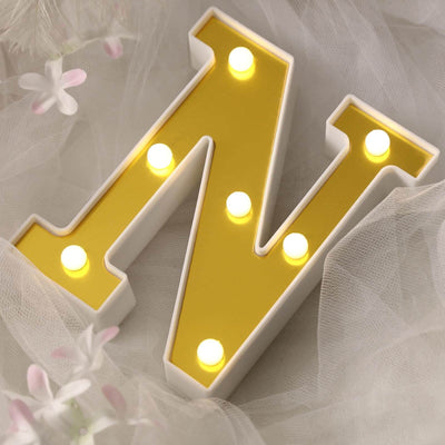 Yellow marquee letter "N" with lights on soft fabric background.
