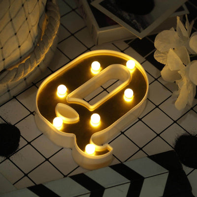Decorative light-up letter "Q" with warm LED bulbs on a patterned surface.