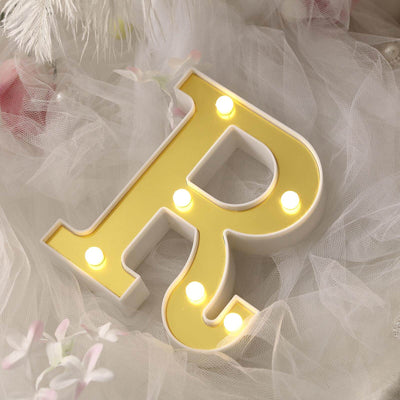 Yellow illuminated letter "R" on soft white fabric background.