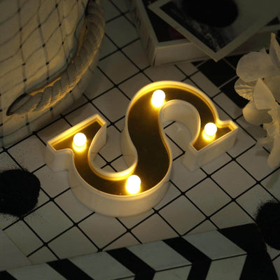 Decorative dollar sign lamp with warm LED lights on a patterned background.