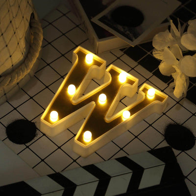 Illuminated letter "W" marquee sign on a patterned surface.