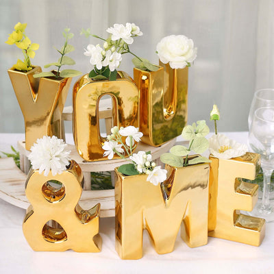 Gold "YOU & ME" letter vases with flowers on a decorative tray.