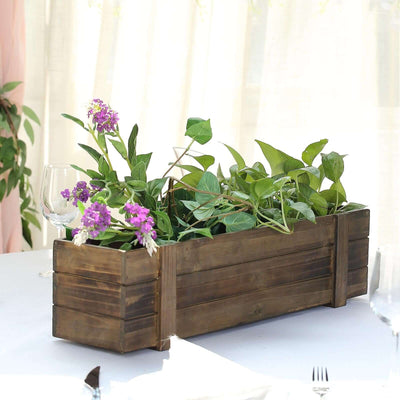 Wooden planter box with green plants and purple flowers on a table.