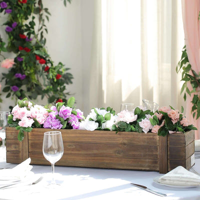 Wooden planter box with pink and purple flowers on a dining table.