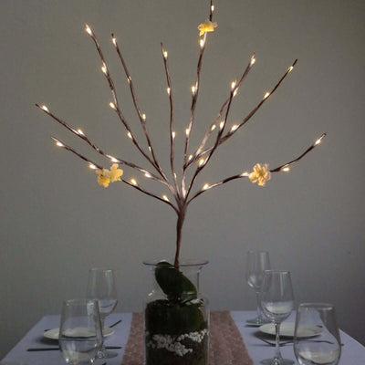 Decorative lighted branch centerpiece with flowers in a glass vase.