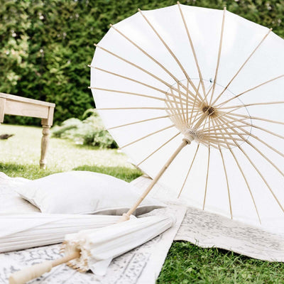 White parasol on a picnic blanket in a garden setting.