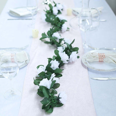 Floral table runner with white roses on a dining table setting.