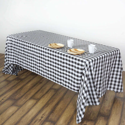 Black and white checkered tablecloth on wooden table with plates and cups.