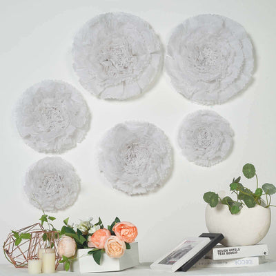 Decorative white paper flowers arranged on a wall with plants and books below.