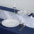 Elegant table setting with white plates and wine glasses on a blue tablecloth.