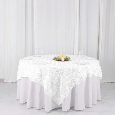 White rose-patterned tablecloth draped over a round table with candles.