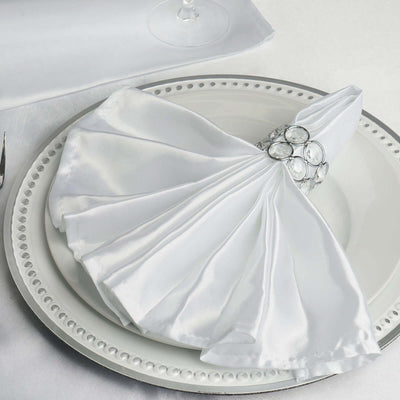 Elegant white napkin folded on a decorative plate with a jeweled napkin ring.