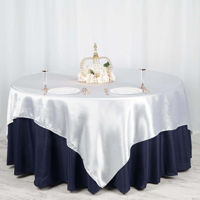 Elegant round table set with silver and navy satin tablecloth, plates, and floral centerpiece.