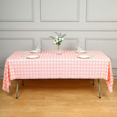 Pink checkered tablecloth on a dining table set with plates and glasses.