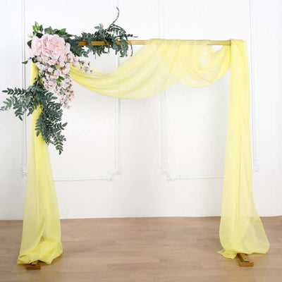 Yellow draped wedding arch with floral accents on a plain backdrop.