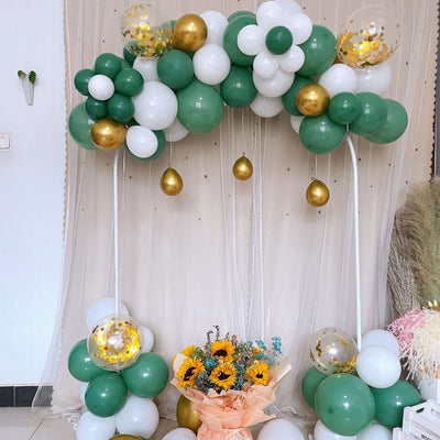 Green and white balloon arch with gold accents and a bouquet of sunflowers.