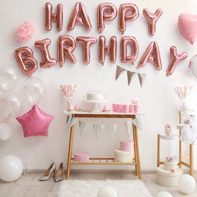 Rose gold "Happy Birthday" balloons with party decorations and a cake display.